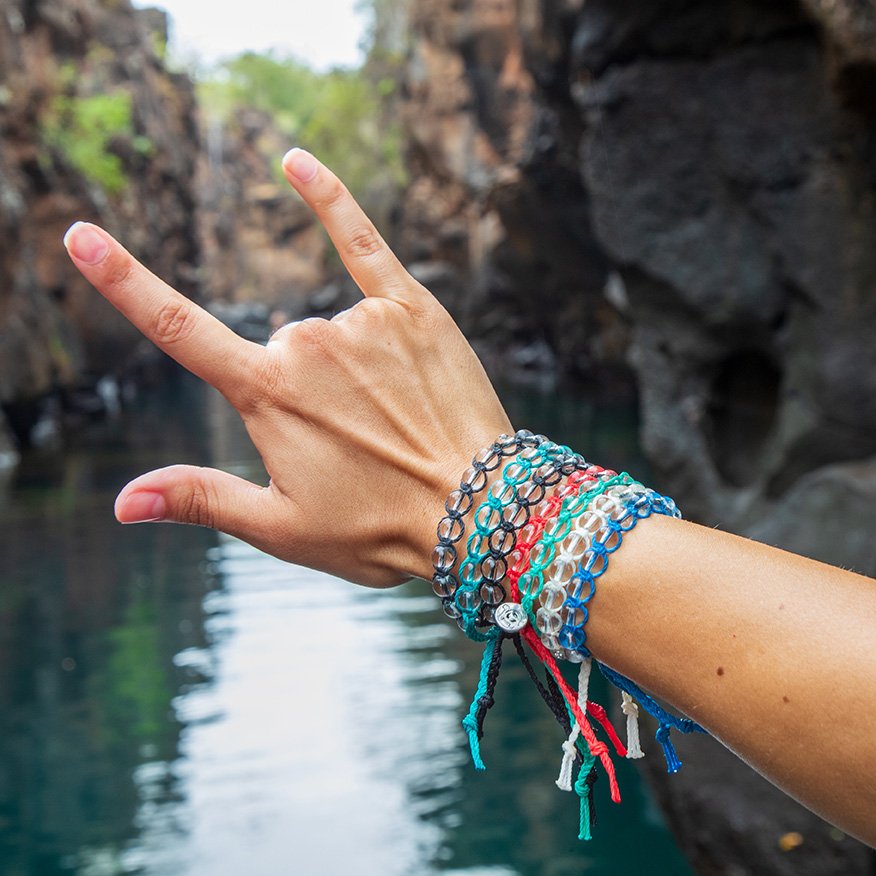 Wrist with Galapagos for Life bracelets over a lagoon